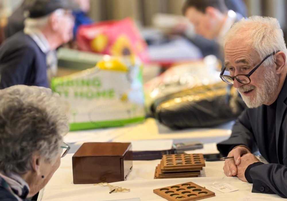 A specialist examining coins with a visitor at a valuation day